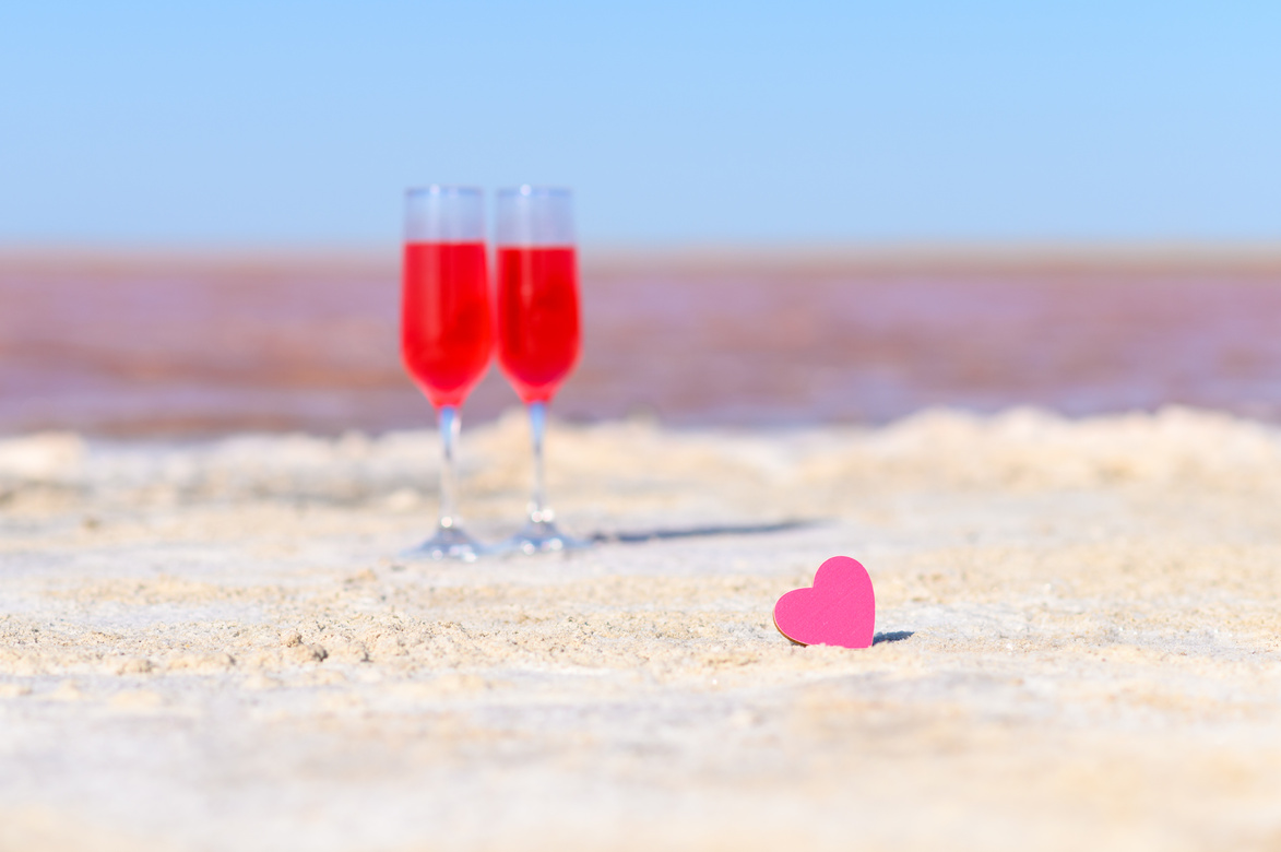 Small pink heart on the background of glasses with rose wine and pink lake. Romantic getaway concept.